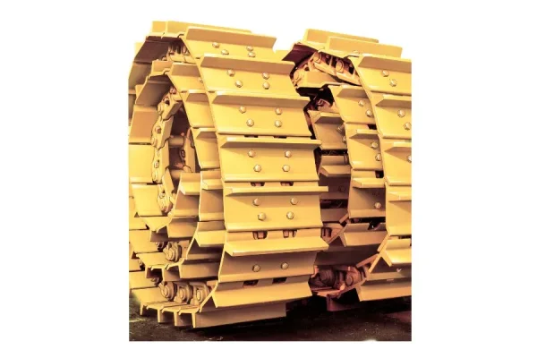 A close-up view of a yellow track link assembly, showcasing its layered, rectangular metal components with visible bolts.